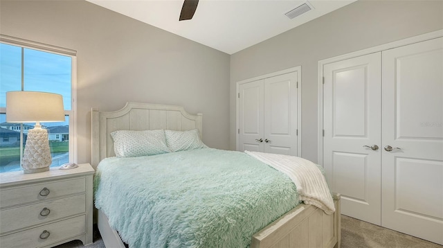 carpeted bedroom featuring multiple closets and ceiling fan