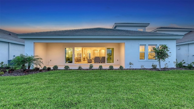back of property featuring a lawn and stucco siding