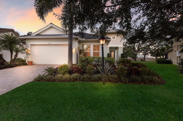 view of front of property featuring decorative driveway, a garage, a yard, and stucco siding
