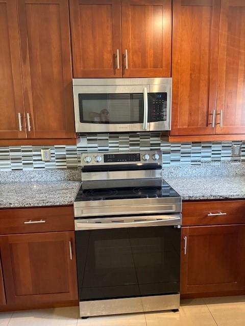 2616 Hidden Lake Dr N Unit A, Sarasota, FL 34237 - kitchen featuring stainless steel appliances, light stone counters, backsplash, and brown cabinets