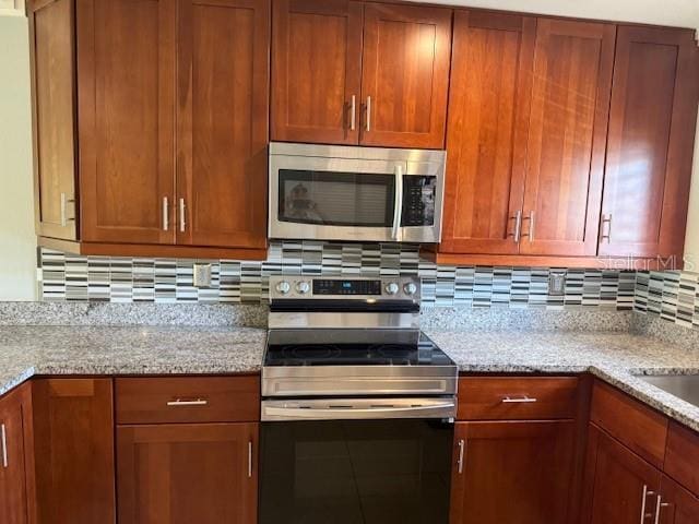 2616 Hidden Lake Dr N Unit A, Sarasota, FL 34237 - kitchen featuring stainless steel appliances, decorative backsplash, light stone counters, and brown cabinetry