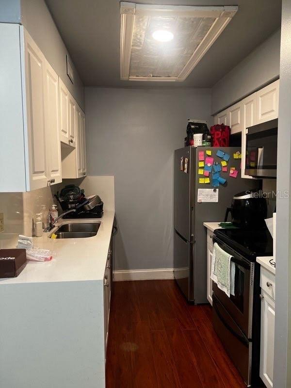 kitchen featuring appliances with stainless steel finishes, a sink, dark wood-style flooring, light countertops, and white cabinets