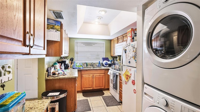 5964 7th Ave W Unit 5964, Bradenton, FL 34209 - kitchen featuring white appliances, stacked washer and clothes dryer, brown cabinetry, a raised ceiling, and light tile patterned floors