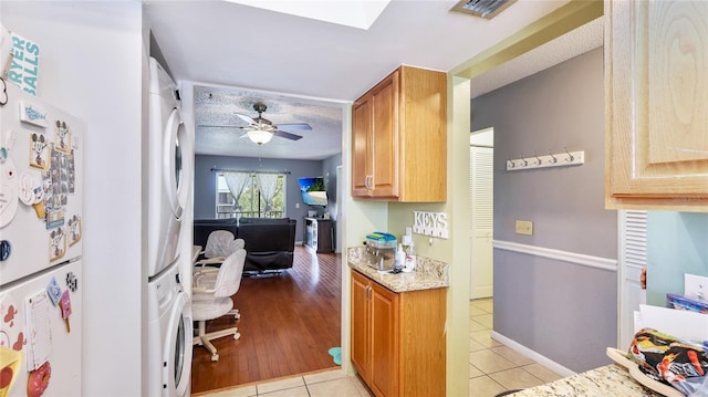 5964 7th Ave W Unit 5964, Bradenton, FL 34209 - kitchen featuring stacked washer / dryer, freestanding refrigerator, light tile patterned floors, a ceiling fan, and light stone countertops