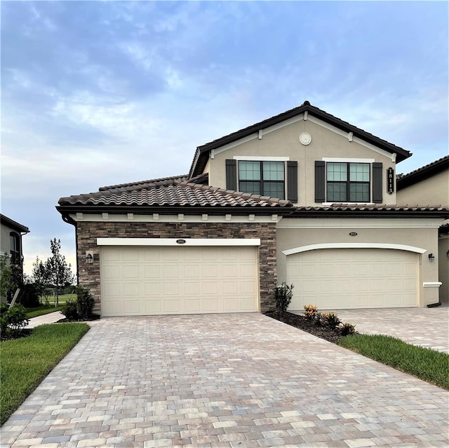 view of front facade featuring stone siding, decorative driveway, stucco siding, and a garage