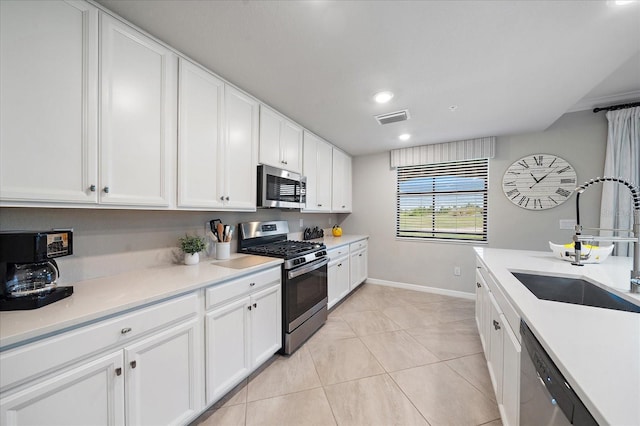 kitchen with appliances with stainless steel finishes, a sink, baseboards, white cabinetry, and light tile patterned flooring
