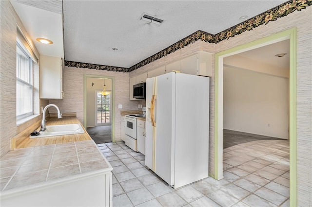 kitchen with white appliances, a sink, white cabinetry, tile countertops, and light tile patterned flooring