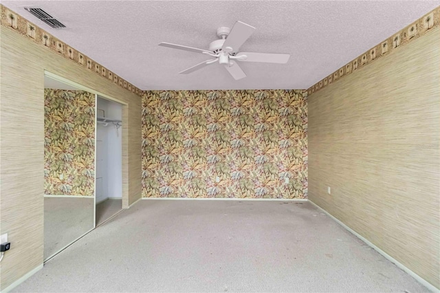 carpeted empty room featuring wallpapered walls, a ceiling fan, baseboards, and a textured ceiling