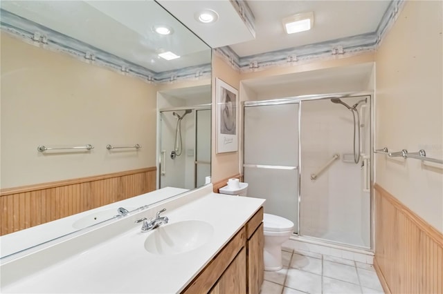 bathroom with a wainscoted wall, a stall shower, toilet, vanity, and tile patterned flooring