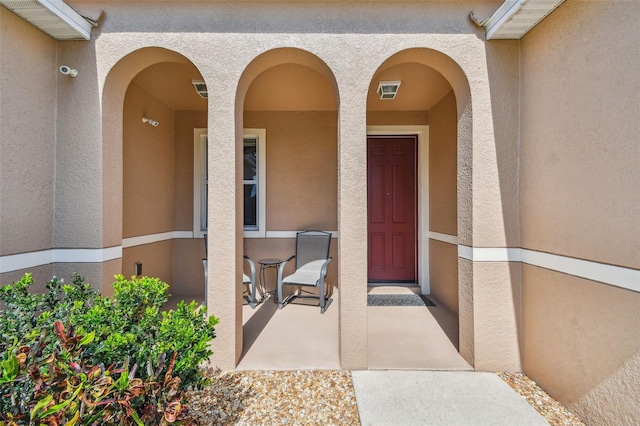 view of exterior entry with stucco siding and a porch