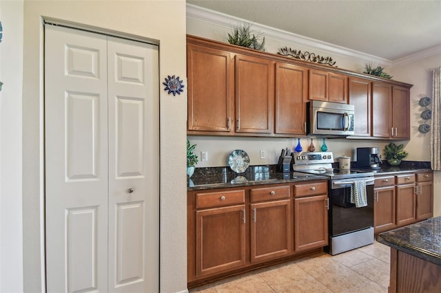 kitchen with stainless steel appliances, dark stone countertops, ornamental molding, brown cabinetry, and light tile patterned floors