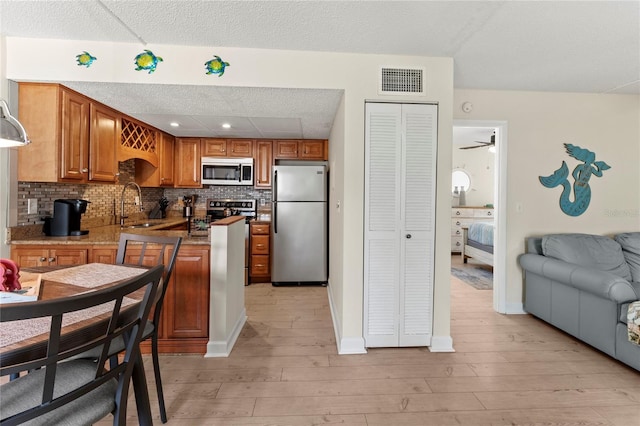 kitchen featuring stainless steel appliances, a sink, light wood-type flooring, backsplash, and open floor plan