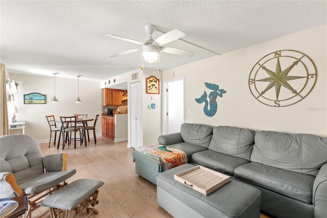 living area with ceiling fan, a textured ceiling, and light wood-style floors