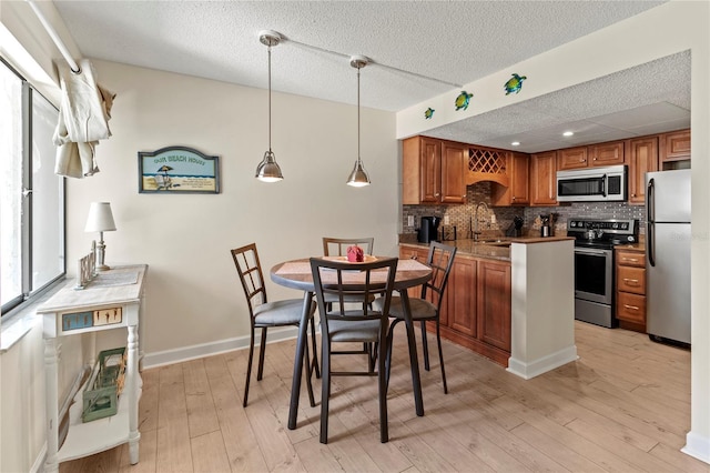 kitchen with stainless steel appliances, brown cabinets, backsplash, light wood-style flooring, and decorative light fixtures