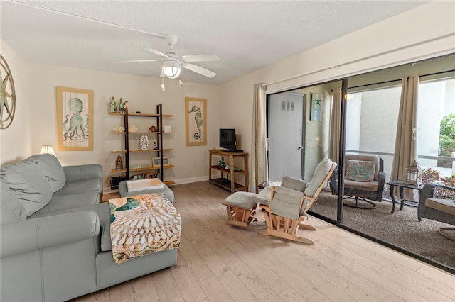 living area with wood-type flooring, a ceiling fan, a textured ceiling, and baseboards