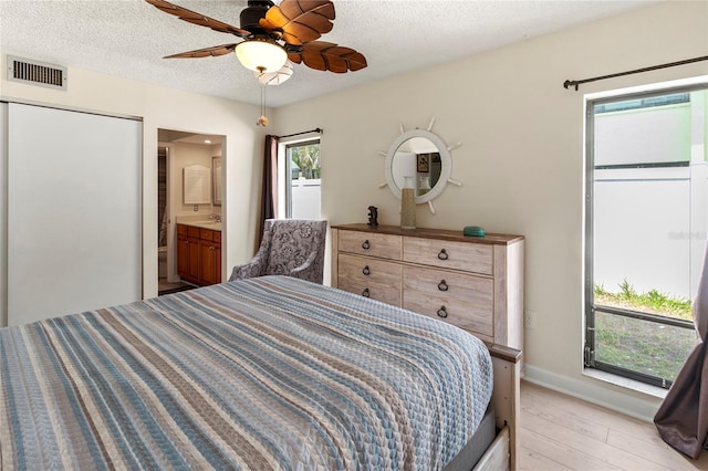 bedroom featuring light wood-style flooring, baseboards, a textured ceiling, ensuite bath, and a ceiling fan