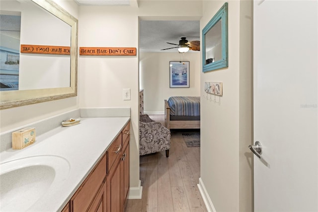 bathroom with hardwood / wood-style floors, a ceiling fan, ensuite bath, vanity, and baseboards