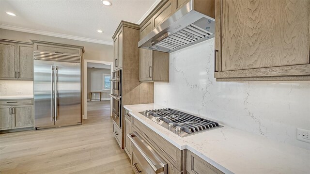 878 Freeling Dr, Sarasota, FL 34242 - kitchen with appliances with stainless steel finishes, wall chimney exhaust hood, light wood-type flooring, tasteful backsplash, and light stone countertops