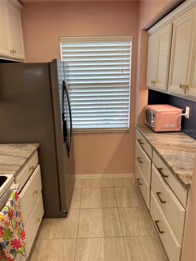 kitchen featuring light tile patterned floors, baseboards, light stone counters, stainless steel fridge, and white cabinets