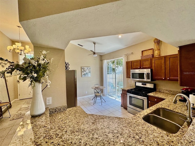 kitchen with appliances with stainless steel finishes, a sink, light tile patterned flooring, light stone counters, and a chandelier