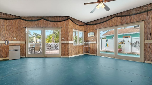 unfurnished living room featuring concrete floors, wood walls, and ceiling fan