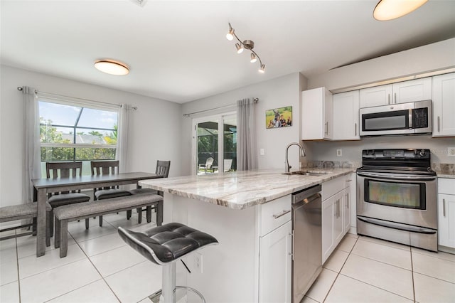 kitchen with appliances with stainless steel finishes, a sink, a peninsula, light tile patterned floors, and plenty of natural light