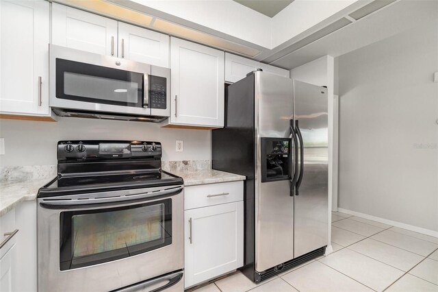 kitchen with appliances with stainless steel finishes, white cabinets, light tile patterned floors, and light stone counters