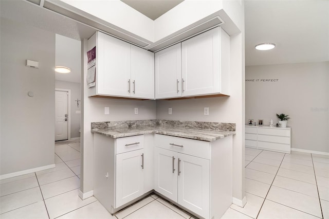 kitchen with light tile patterned flooring, baseboards, white cabinetry, and light stone countertops