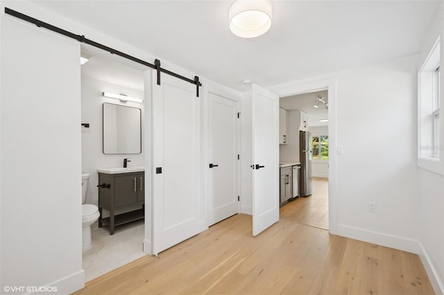 2655 Bay St, Sarasota, FL 34237 - unfurnished bedroom with light wood finished floors, a barn door, freestanding refrigerator, a sink, and baseboards