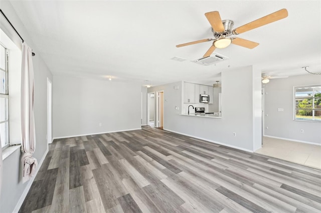 unfurnished living room featuring a ceiling fan, wood finished floors, a sink, and baseboards