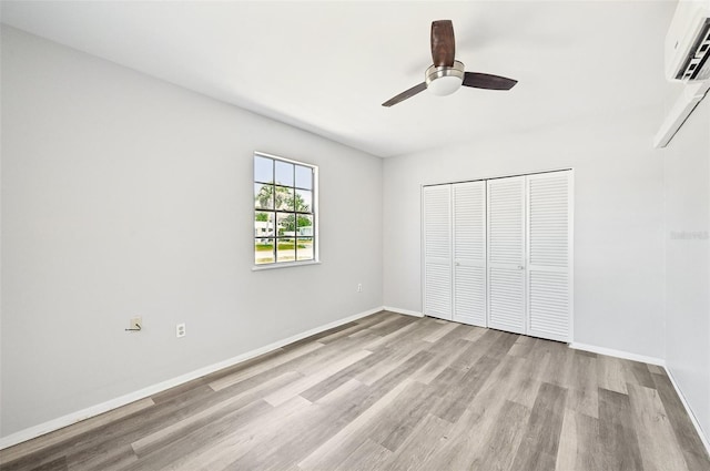 unfurnished bedroom with light wood-style flooring, a wall unit AC, baseboards, a closet, and ceiling fan