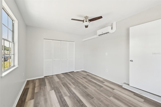 unfurnished bedroom with a wall mounted air conditioner, a closet, wood finished floors, and baseboards