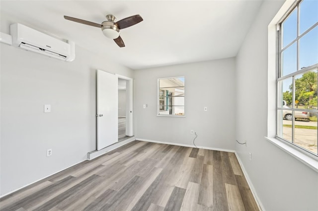 unfurnished bedroom with a wall mounted air conditioner, wood finished floors, ceiling fan, and baseboards