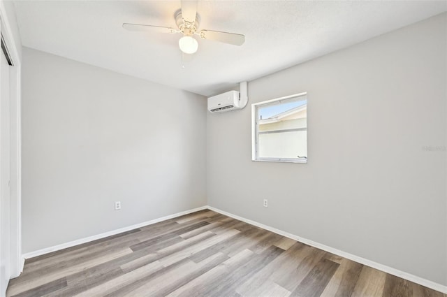 unfurnished room with a wall unit AC, wood finished floors, a ceiling fan, and baseboards