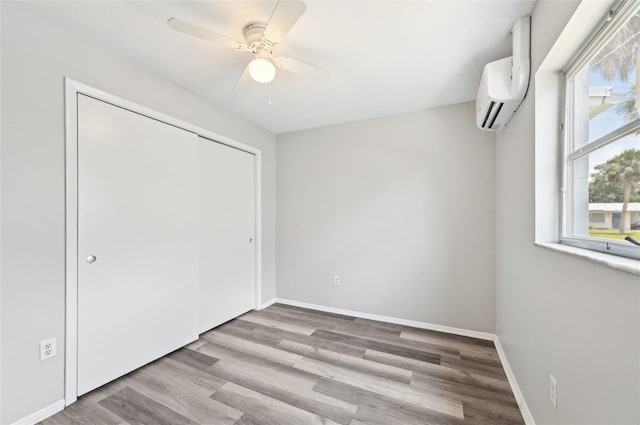unfurnished bedroom with a wall unit AC, wood finished floors, and baseboards