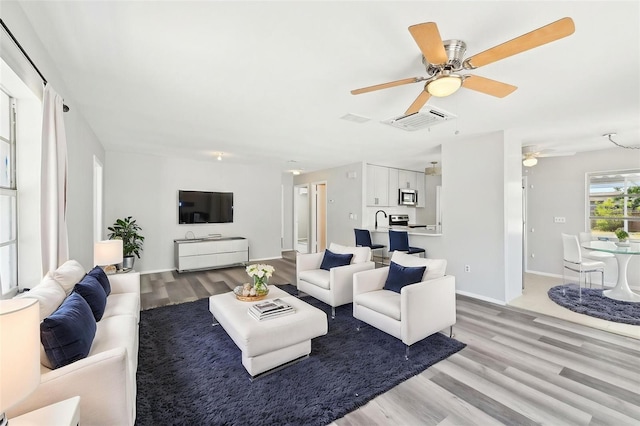 living area featuring light wood-style flooring, ceiling fan, and baseboards