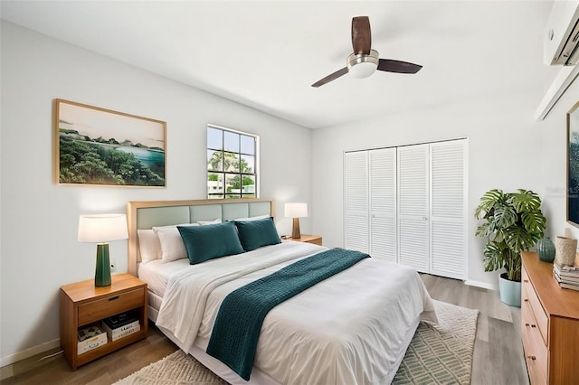 bedroom with an AC wall unit, a closet, light wood-style floors, baseboards, and a ceiling fan