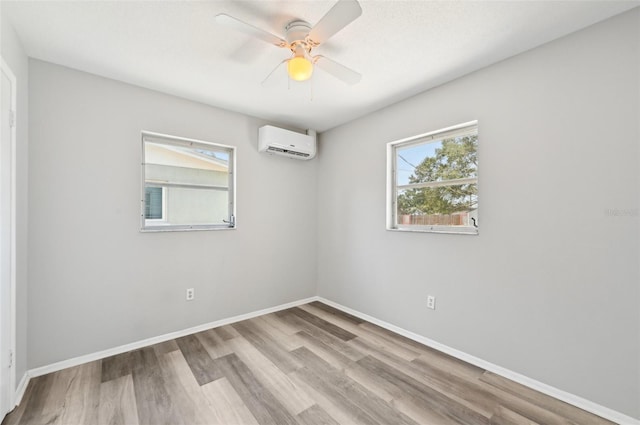 unfurnished room with a wall unit AC, wood finished floors, a ceiling fan, and baseboards