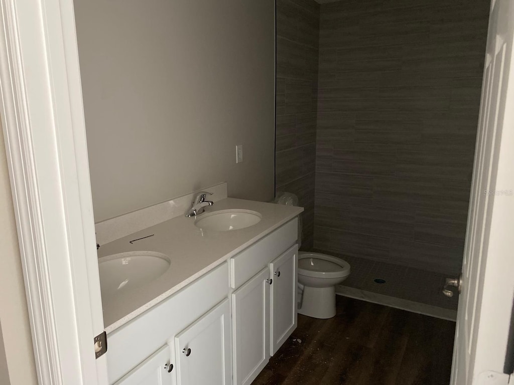 bathroom featuring a stall shower, wood finished floors, double vanity, and toilet