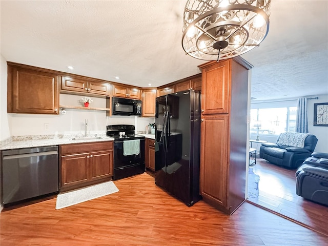 kitchen featuring black appliances, open floor plan, light wood finished floors, a textured ceiling, and a sink