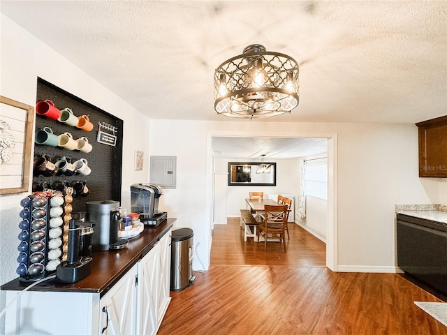 dining area featuring light wood-style flooring, a chandelier, a textured ceiling, baseboards, and electric panel