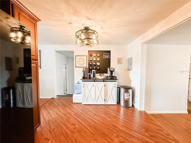 bar featuring light wood finished floors, baseboards, a textured ceiling, and a chandelier