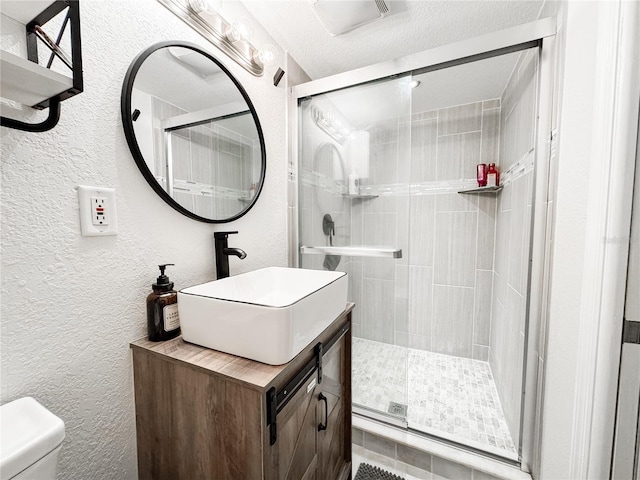 full bath with a textured wall, toilet, a stall shower, and vanity