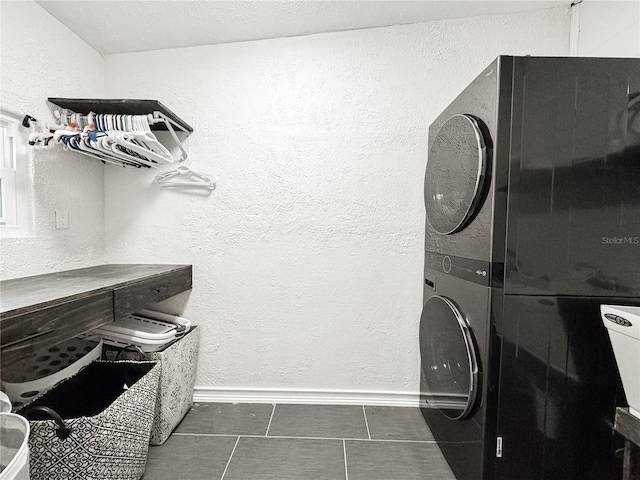 clothes washing area with stacked washing machine and dryer, baseboards, dark tile patterned floors, and a textured wall