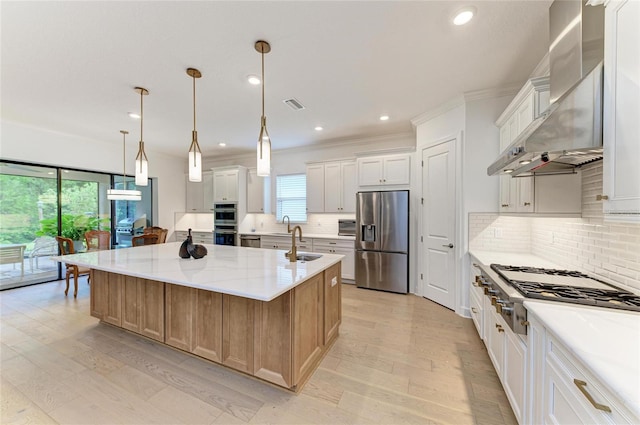 kitchen with appliances with stainless steel finishes, light wood finished floors, a sink, decorative backsplash, and a spacious island