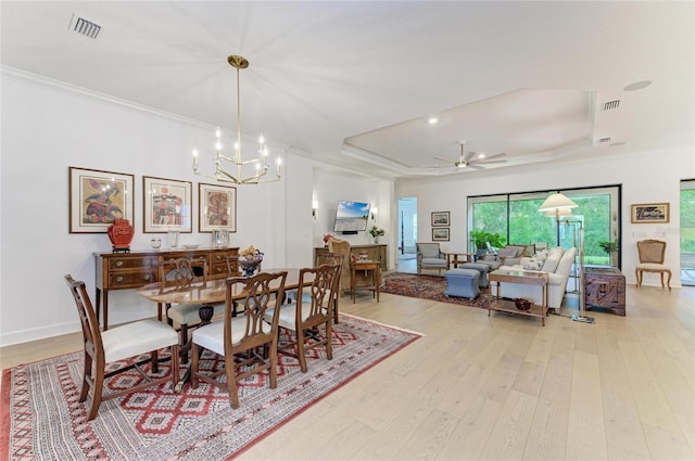 dining space featuring a tray ceiling, light wood-style floors, crown molding, a chandelier, and a ceiling fan