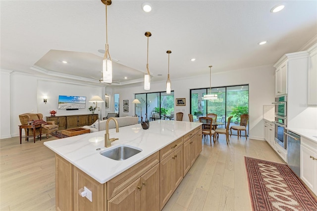 kitchen featuring a sink, appliances with stainless steel finishes, ornamental molding, light wood-type flooring, and a center island with sink