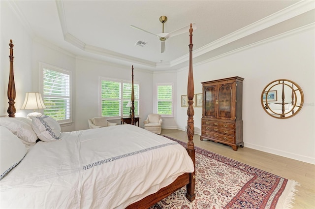 bedroom featuring crown molding, a raised ceiling, light wood-style floors, baseboards, and a ceiling fan