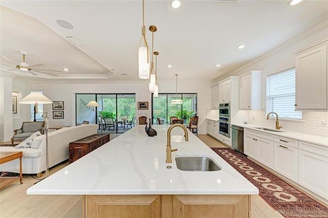 kitchen featuring a sink, stainless steel appliances, a large island with sink, open floor plan, and ornamental molding