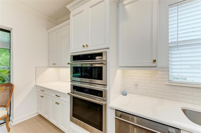 kitchen with appliances with stainless steel finishes, tasteful backsplash, crown molding, and white cabinets